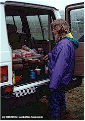 Susanne steht im Regen am Kochherd im Heck des Wagens